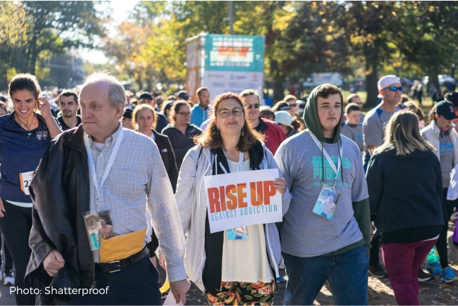 People walking with one person holding sign that reads, "Rise Up Against Addiction"