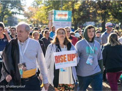 People walking with one person holding sign that reads, "Rise Up Against Addiction"