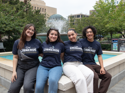 Four Cisneros Scholars sit by a fountain facing the camera and wearing navy shirts