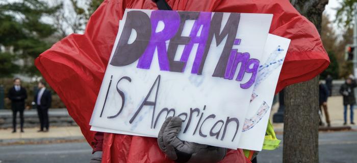Person in Red Jacket holds sign that says "Dreaming is American"