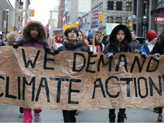 Student protesting with sign that reads, "We demand climate action now"